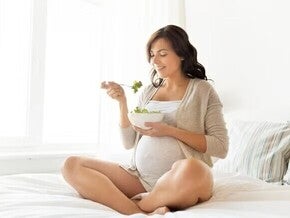 Pregnant woman eating salad on her bed