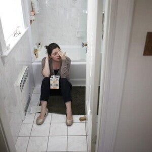 A woman sitting in the bathroom dealing with morning sickness