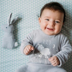 A toddler smiling in bed without any baby’s tummy problems