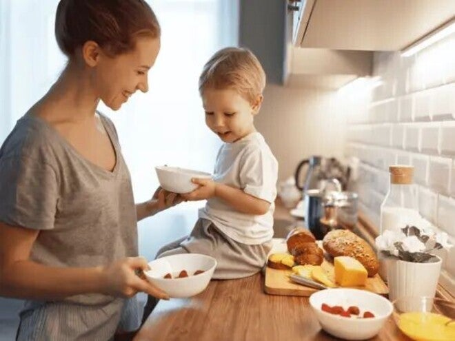 Mother with her toddler in the kitchen with fruits, bread, and cheese.