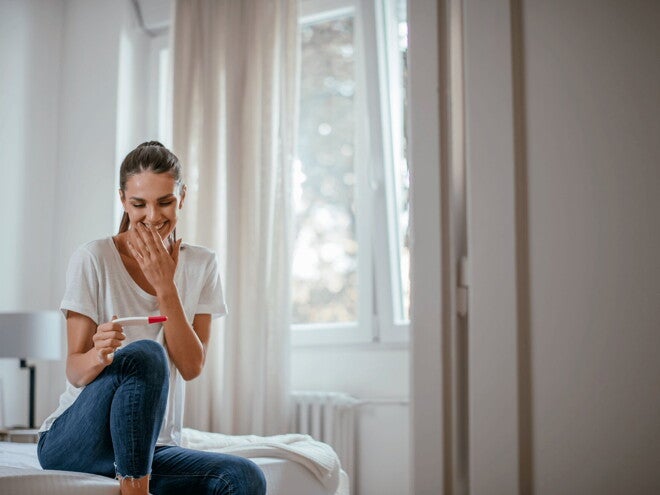 The first trimester is an important part of the development of a baby. A woman smiling at a pregnancy test in the early first trimester.