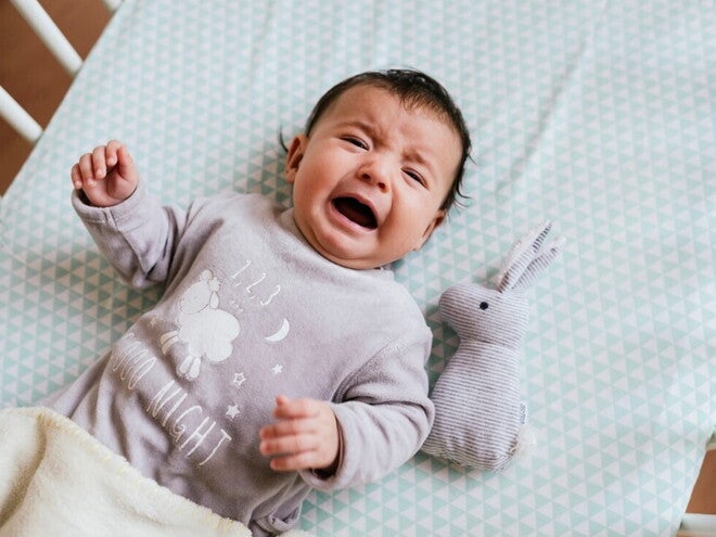 Learn how to understand why babies cry with this guide. A baby crying inside their crib.