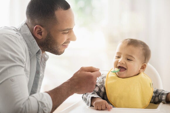 Consult your pediatrician on how to introduce your baby’s first foods. A father giving his baby his first food.