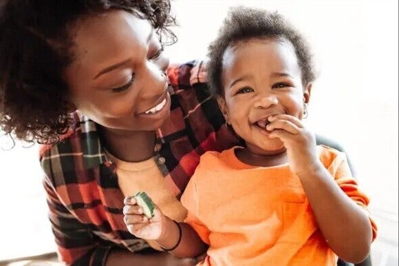 A woman teaching her baby how to feed herself.