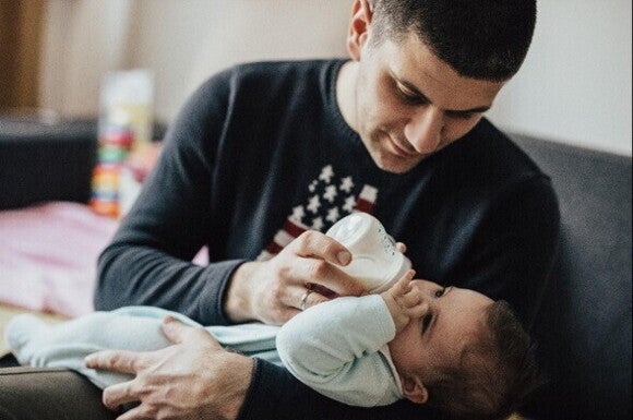 A father feeding his child with milk from a breast pump 