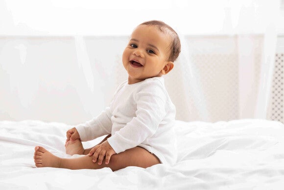Baby sitting on a bed smiling