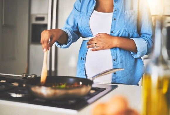 Pregnant woman cooking a healthy meal while touching her belly