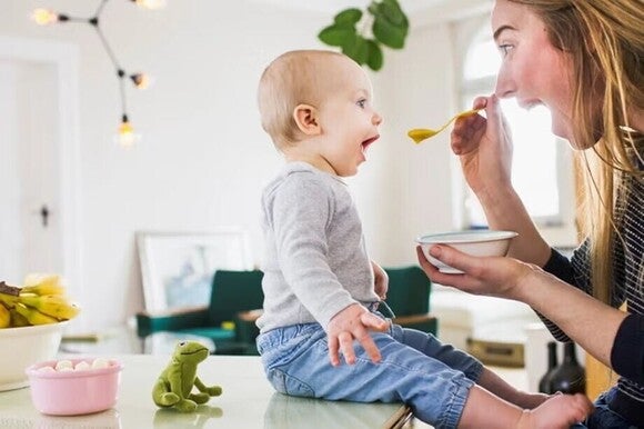 Baby with his mom, being feed with puree