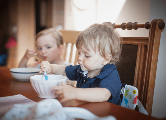 Eating together as a family is part of the social development of a kid Two toddlers eating together at home.